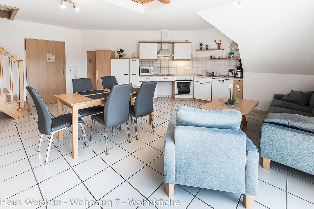 Offene Wohnküche der Wohnung 7 mit Küchenzeile, großem Essplatz und Blick in Richtung Eingang. Die Küche besitzt laut „Reisen für Alle“ 200 cm schmalsten Durchgang und 450 × 300 cm Bewegungsfläche vor Herd und Spüle.