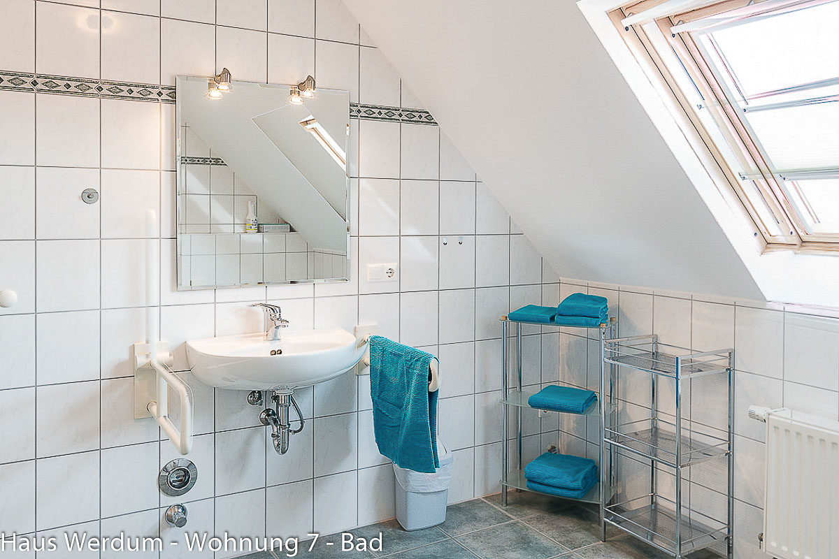 Frontalansicht des Waschplatzes in Wohnung 7 mit offenem Waschbecken, Spiegel und zwei seitlichen Stützgriffen. Reisen für Alle weist 333 × 212 cm Bewegungsfläche vor dem Waschbecken und 85 cm Höhe der Waschbeckenoberkante aus.
