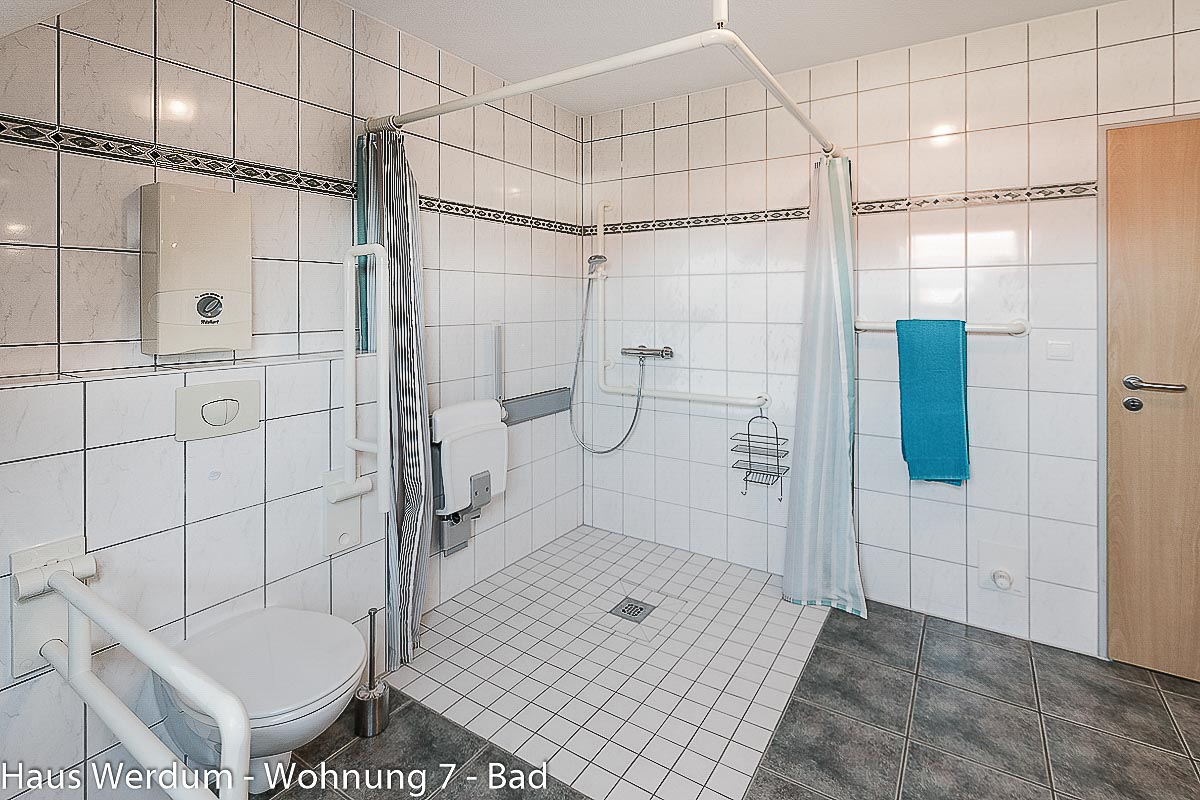 Bodengleiche Dusche der Wohnung 7 mit Klappsitz, Haltegriffen, Handbrause und Bodenablauf. Laut Reisen für Alle beträgt der Höhenunterschied 0 cm und die Bewegungsfläche in der Dusche 150 × 161 cm.