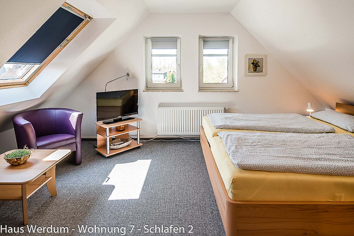 Schlafzimmer 2 der Wohnung 7 im Dachgeschoss mit zwei Einzelbetten als Doppelbett, TV und Sitzecke. Der Raum ist ausschließlich über die Holztreppe erreichbar und daher nicht stufenlos, nicht barrierefrei und nicht rollstuhlgerecht zugänglich.