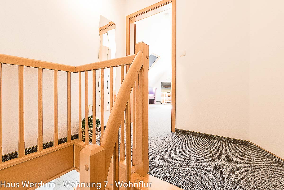 Holztreppe und Wohnflur der Wohnung 7 vor dem Zugang zu Schlafzimmer 2. Die Treppe ist der einzige Zugang zum oberen Schlafraum; Schlafzimmer 2 ist damit nicht stufenlos, nicht barrierefrei und nicht rollstuhlgerecht erreichbar.
