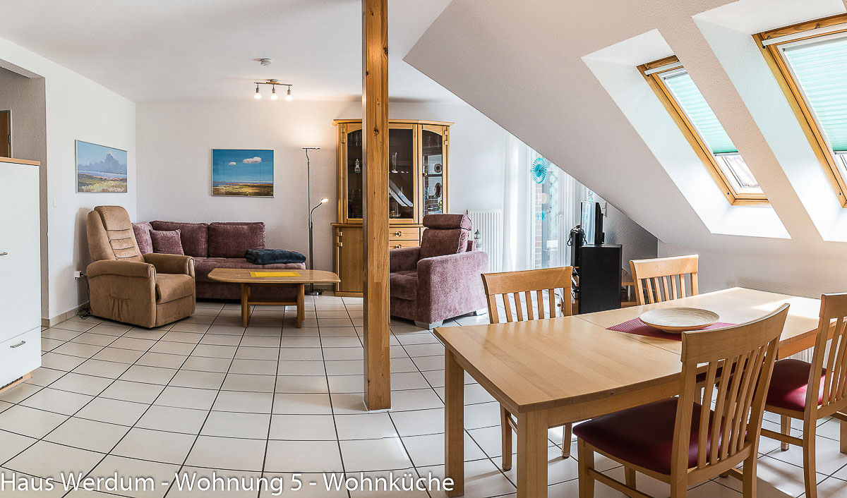 Gesamtansicht des barrierefreien Wohn- und Essbereichs in Wohnung 5 im Haus Werdum mit Holzesstisch, zwei großen Dachfenstern, einer Polstercouch, einem seniorengerechten Sessel und einem schwellenlosen Fliesenboden mit weiten Durchgängen