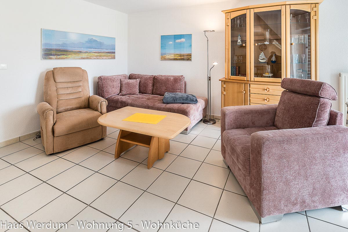 Gemütlicher Wohnbereich in Wohnung 5 im Haus Werdum mit Eckcouch, zwei gepolsterten Sesseln, Holzcouchtisch und heller Vitrine auf schwellenlosem Fliesenboden mit ausreichend Bewegungsfläche Rollstuhlfahrer und für Gehhilfen