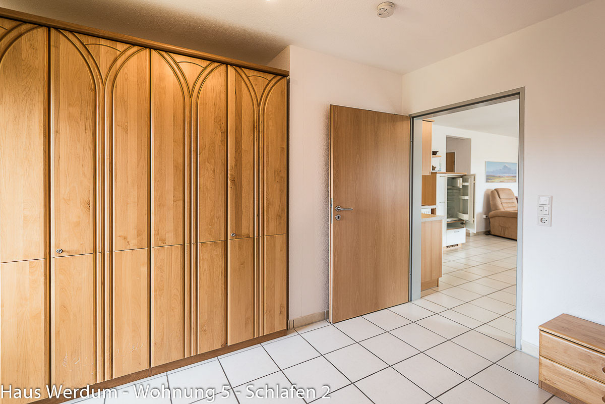 Großer Holz-Kleiderschrank im Schlafzimmer von Wohnung 5 im Haus Werdum mit stufenlosem Übergang durch die geöffnete Tür in den Wohnbereich