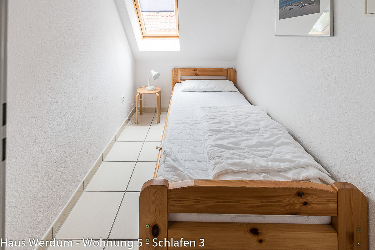 Schmaler Schlafraum in Wohnung 5 im Haus Werdum mit Holzbett, Fliesenboden und Dachfenster. Aufgrund geringer Durchgangsbreite nicht rollstuhlgerecht
