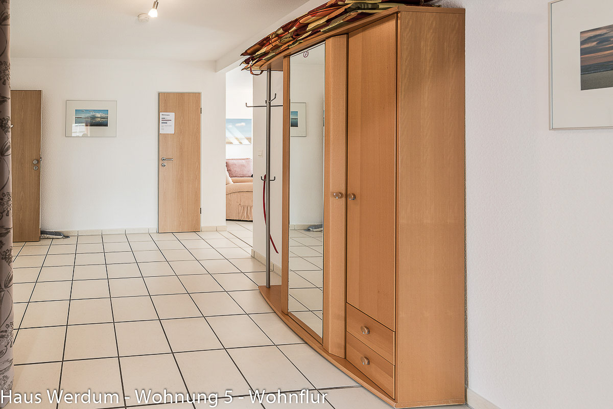 Seitenansicht des schwellenlosen Wohnflurs in Wohnung 5 im Haus Werdum mit heller Fliesung, einer Holzgarderobe und breiten Zimmertüren aus Holz